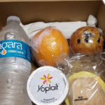 prepackaged breakfast box with water bottle, orange, yogurt and muffin