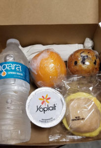 prepackaged breakfast box with water bottle, orange, yogurt and muffin