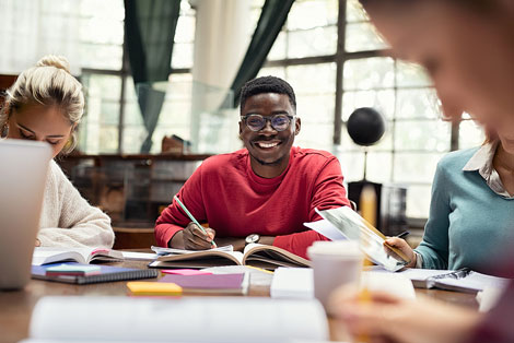 Happy college student sitting in library with friends